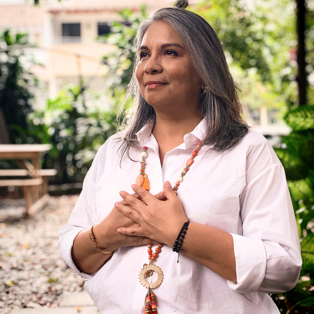 Claudia Palacio en un jardín, con las manos sobre el corazón